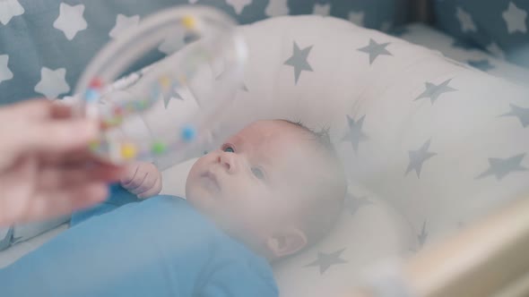 Mommy Shows Rattle with Beads To Cute Baby in Cocoon