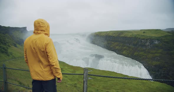 Male Tourist Wearing Yellow Raincoat at Gullfoss Waterfall on Iceland in Icelandic Nature