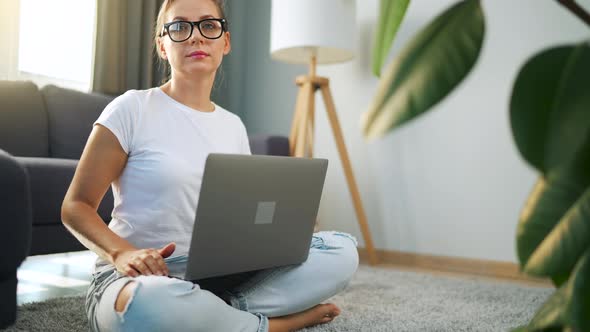 Portrait of a Woman with Glasses Looking at the Camera Over a Laptop in the Interior of a Cozy