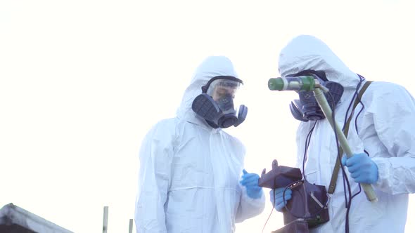 Two Scientists in Protective Suits and Masks and Make Measurements of Radiation Against the