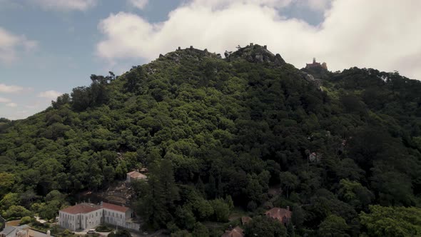 Aerial ascending shot of Sintra hills covered with lush green forest and mountaintop castle