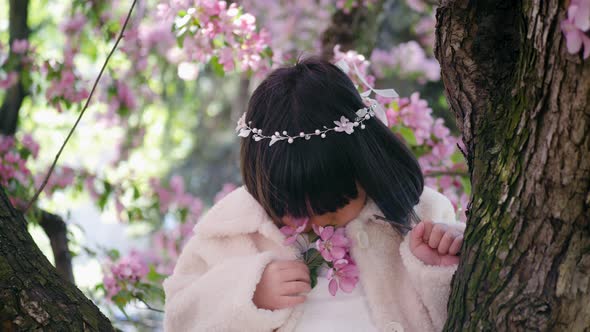 Korean Girl in a White Light Fur Coat and a Headband Sitting on a Tree Branch in a Garden with