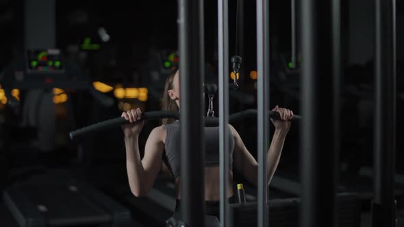 Young Female in the Gym Lifting Blocks on Blocks Machine Strength Training on a Gym Equipment Night