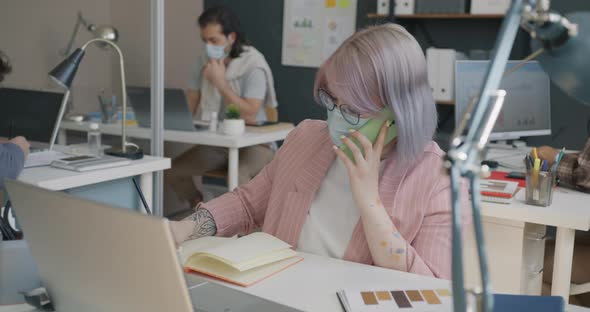 Female Employee Wearing Face Mask Chatting on Mobile Phone Indoors at Workplace