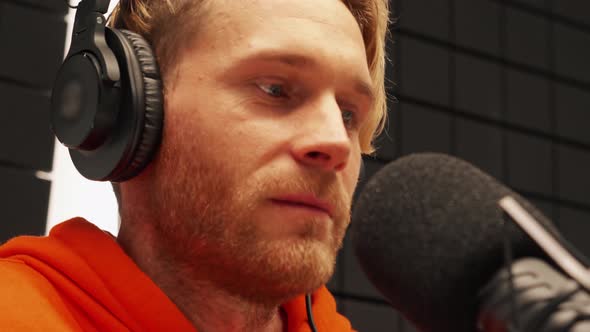 Pensive young man talking into microphone while recording radio show