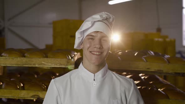 Baker in Uniform Raises a Large Loaf of Bread with Image of Smile at Face Level
