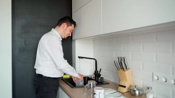 Smiling man washing dishes in the sink in a modern white kitchen at home