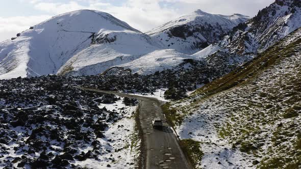 Aerial of Car Driving on Dirt Road Along the Snow Covered Mountains in Iceland