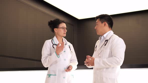 Asian Doctor Communicates with Female Surgeon Discussing in Clinic