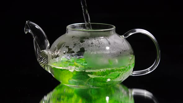 Pouring Hot Water Into a Glass Teapot on a Black Background, Green Mint Tea