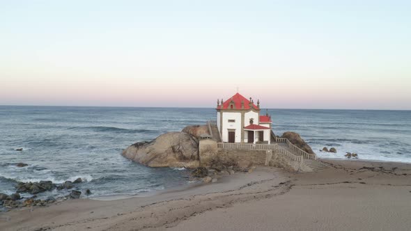 Capela Senhor da Pedra most beautiful chapel drone aerial view on a beach with waves crashing