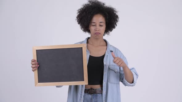 Young Stressed African Woman Holding Blackboard and Giving Thumbs Down