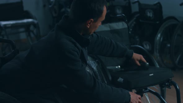 Side View of One American Male Workers in a Workshop at a Factory Making Wheelchairs Sitting at a