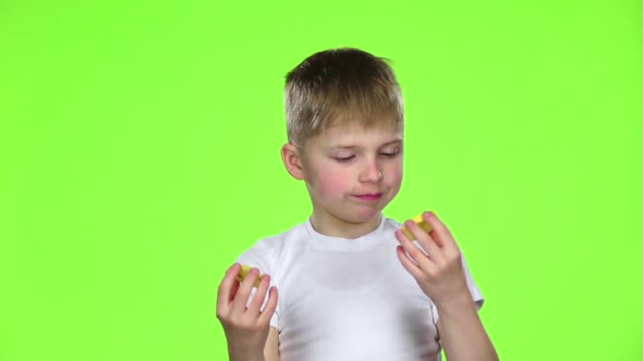 Small Boy Holds a Slice of a Lemon Licks and Curls From Acid. Green Screen. Slow Motion