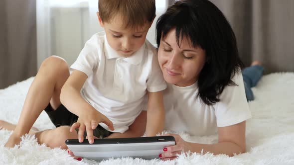 Mom and Little Boy Play the Game or Use the App for Kids on the Tablet.