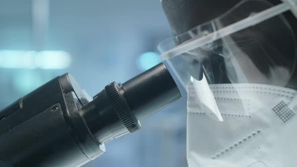 Black Lab Scientist in Protective Uniform Using Microscope