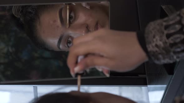 Young Woman Using Concealer To Shape Eyebrow Looking In Mirror. Vertical Video, Locked Off