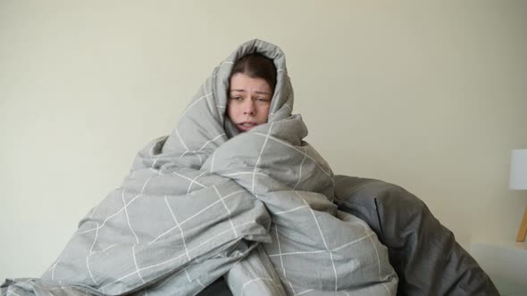 woman freezes in bed and tries to keep warm by wrapping herself in a blanket