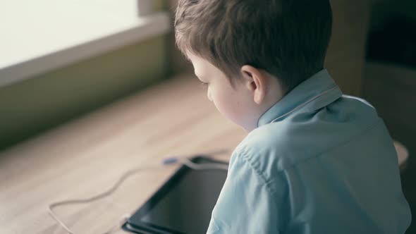 CU Slow Motion Child a Schoolboy Sits at a Table and Thinks That There is a Tablet Computer on the