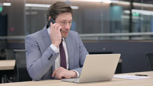 Middle Aged Businessman with Laptop Talking on Smartphone 