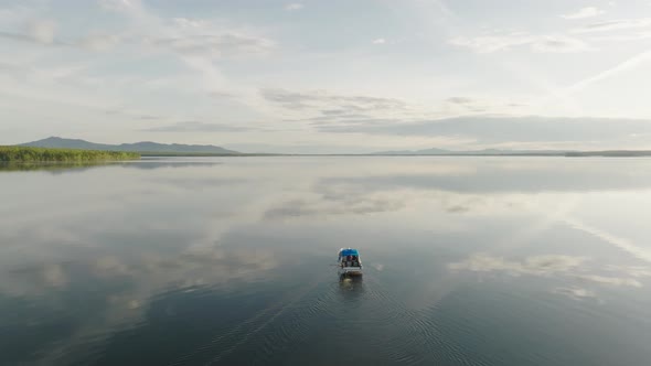 A motorboat putters along flat calm lake Ascending aerial shot