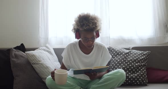 Latin American Woman with Afro Hair Sitting on the Sofa at Home Reading While Drinking Coffee
