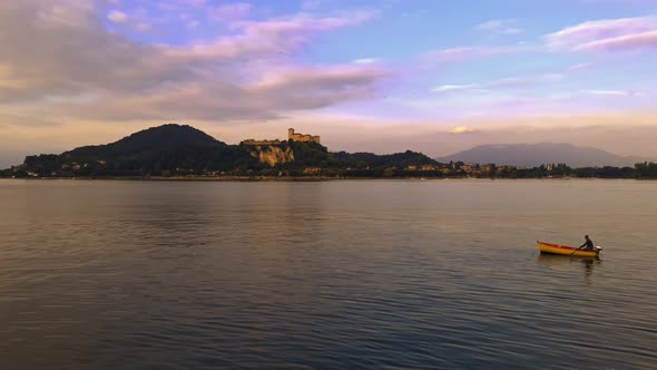 Fisherman slowly rowing small fishing boat on calm lake waters of Maggiore lake in Italy. Slow-motio