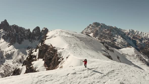 Cinematic circling drone shot of hiker walking along a steep snowy ridge