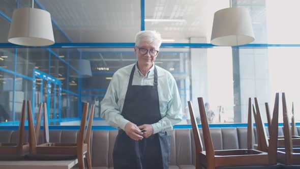 Mature Small Business Owner Arranging Apron Walking in Closed Cafe