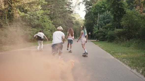 Group of Four Skaters Ride Through the Park with a Smoke Bomb Attached to the Board