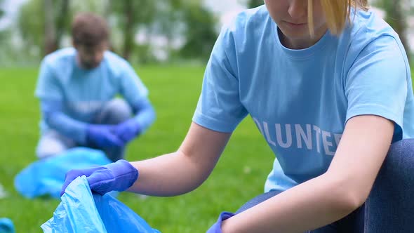 Young Female Volunteer Picking Litter in Park, Smiling on Camera, Save Nature