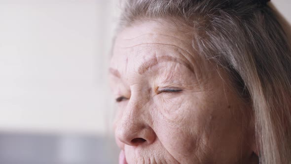 Close Up on Blue Sad Eyes of Lonely Elderly Woman Looking Through the Window