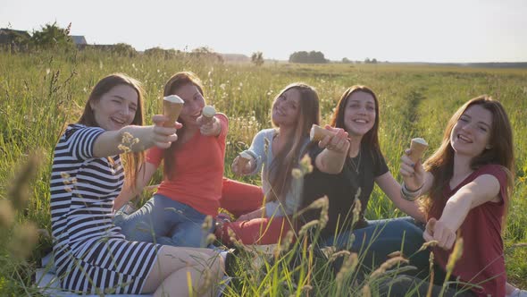 Five Young Schoolgirls Eat and Demonstrate Ice Cream on the Meadow on a Warm Summer Day