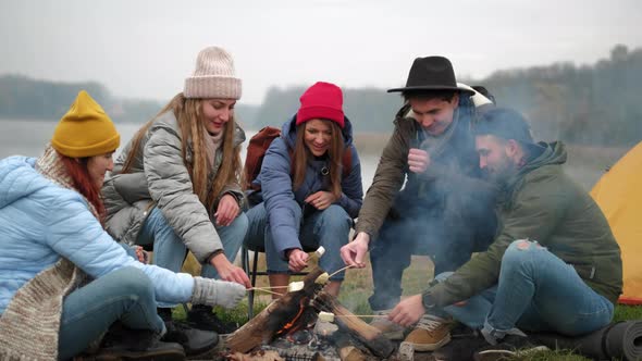 Hungry Travelers Are Cooking Marshmallow on Fire and Eating It From Sticks During Conversation