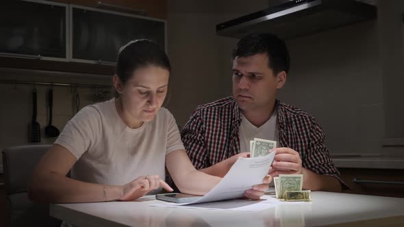 Upset Young Couple Calculating Taxes and Payments on Kitchen at Night