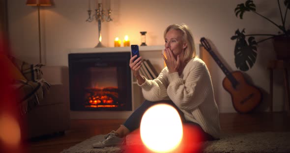 Happy Senior Woman with Smartphone Having Video Call and Waving Hand at Home in Evening