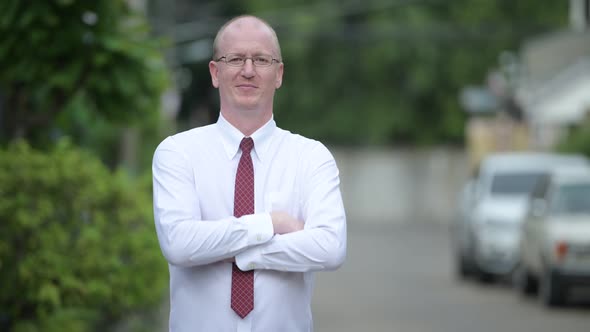 Happy Mature Bald Businessman Smiling with Arms Crossed Outdoors