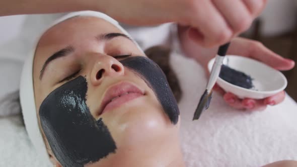 Caucasian woman lying back while beautician gives her a face mask