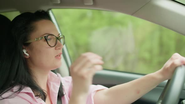 The Girl is Driving a Car and Puts on a Headphone