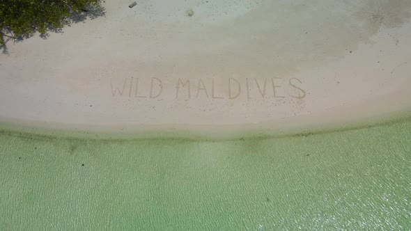 "Wild Maldives" inscription on the sand. Against the background of green trees, white sand, and the