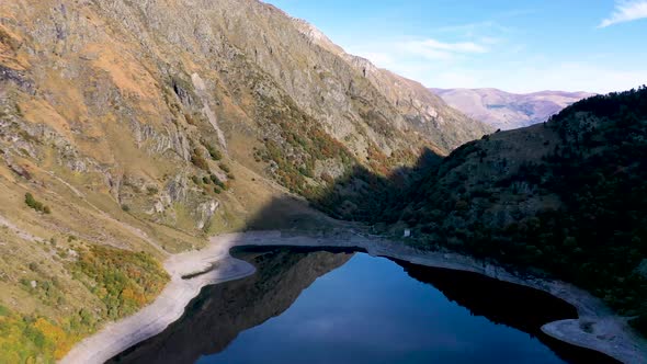 Lac d'Oô dam lake in the French Pyrenees with low water level in the walls, Aerial high altitude fly