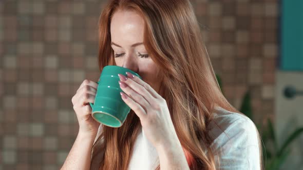 Caucasian woman enjoys drinking morning coffee from a cup in the home kitchen