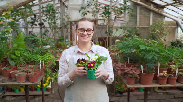 Young Woman Holds Out Pots of Flowers and Smiles