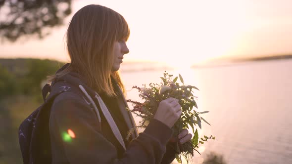 Beautiful Young Woman with a Bouquet of Wildflowers on the Coast at Sunset