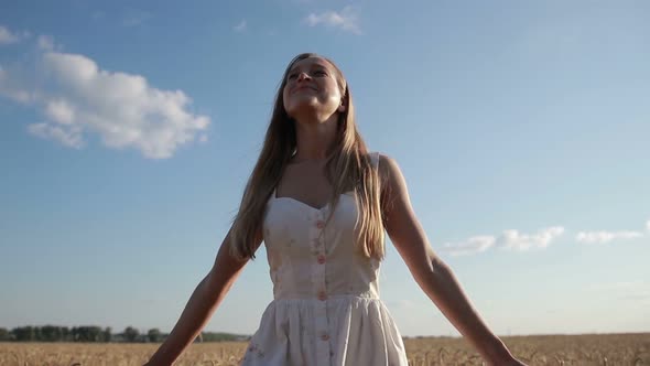 Smiling Girl Walking in Spikes of Wheat Field