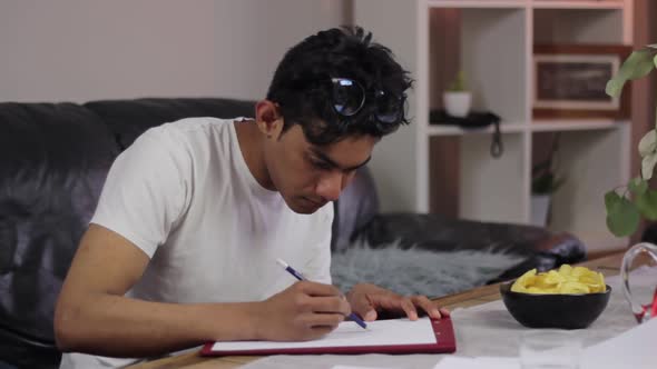 Focused Indian student studies at home for exams, highlighting on paper