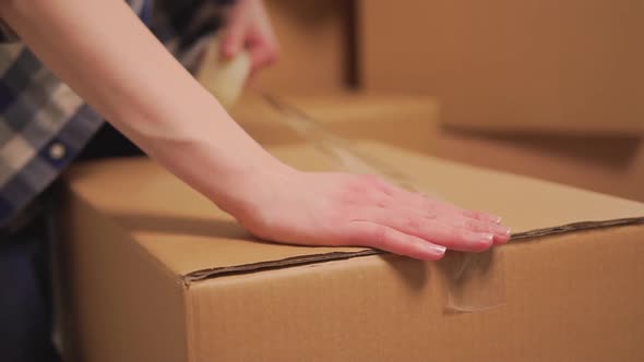 The Woman's Hands Cover the Cardboard Moving Box with Duct Tape