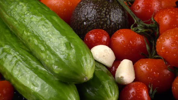 Cherry tomatoes, cucumbers, garlic, avocado and red onion on a black background in water drops