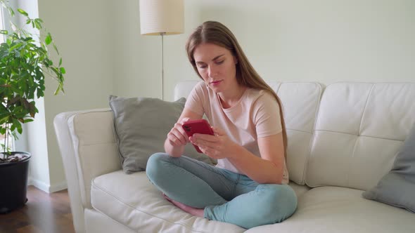 Young Teenage Woman in Headphones Using Smartphone Rest on Sofa at Home