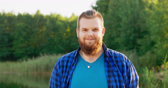 Portrait of a Smiling Young Man with a Red Beard Outdoors in a Forest Near a Lake